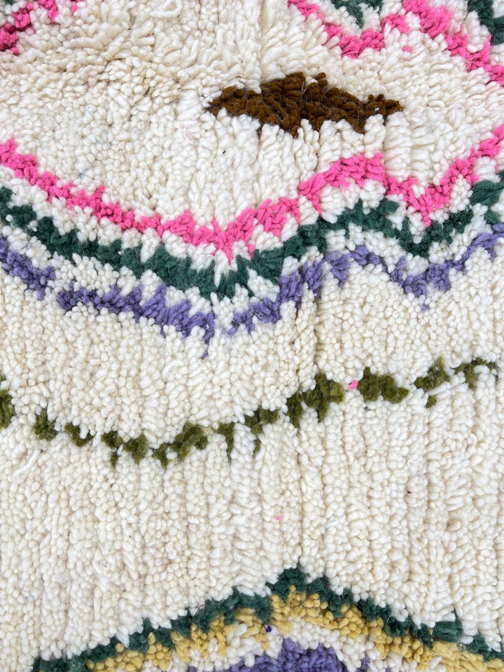 Handmade Moroccan runner rug with colorful geometric and tribal motifs on a white wool background, crafted by Berber artisans.