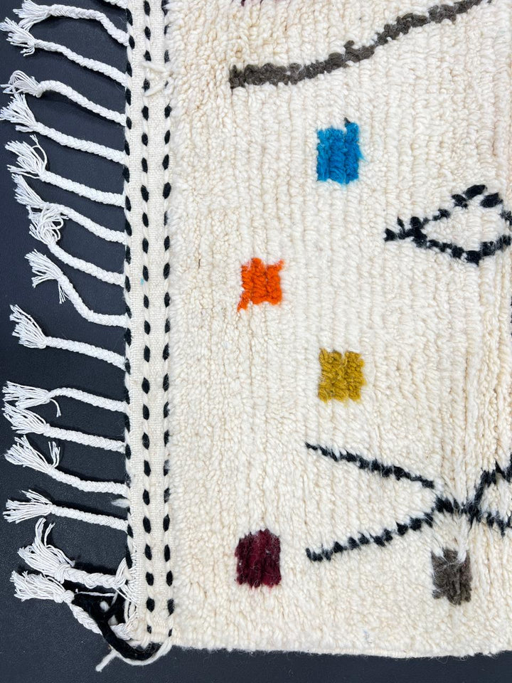 Handmade Moroccan runner rug with colorful geometric symbols, abstract lines, and dotted accents on a white wool background.