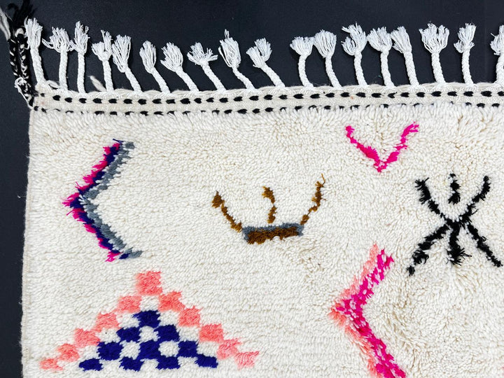 Handwoven Moroccan wool rug with cream background and colorful geometric Berber motifs in pink, blue, green, and yellow