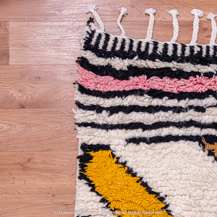 Colorful Abstract Handmade Moroccan Rug with Pink, Yellow, Black Stripes, and Tassels on a Hardwood Floor