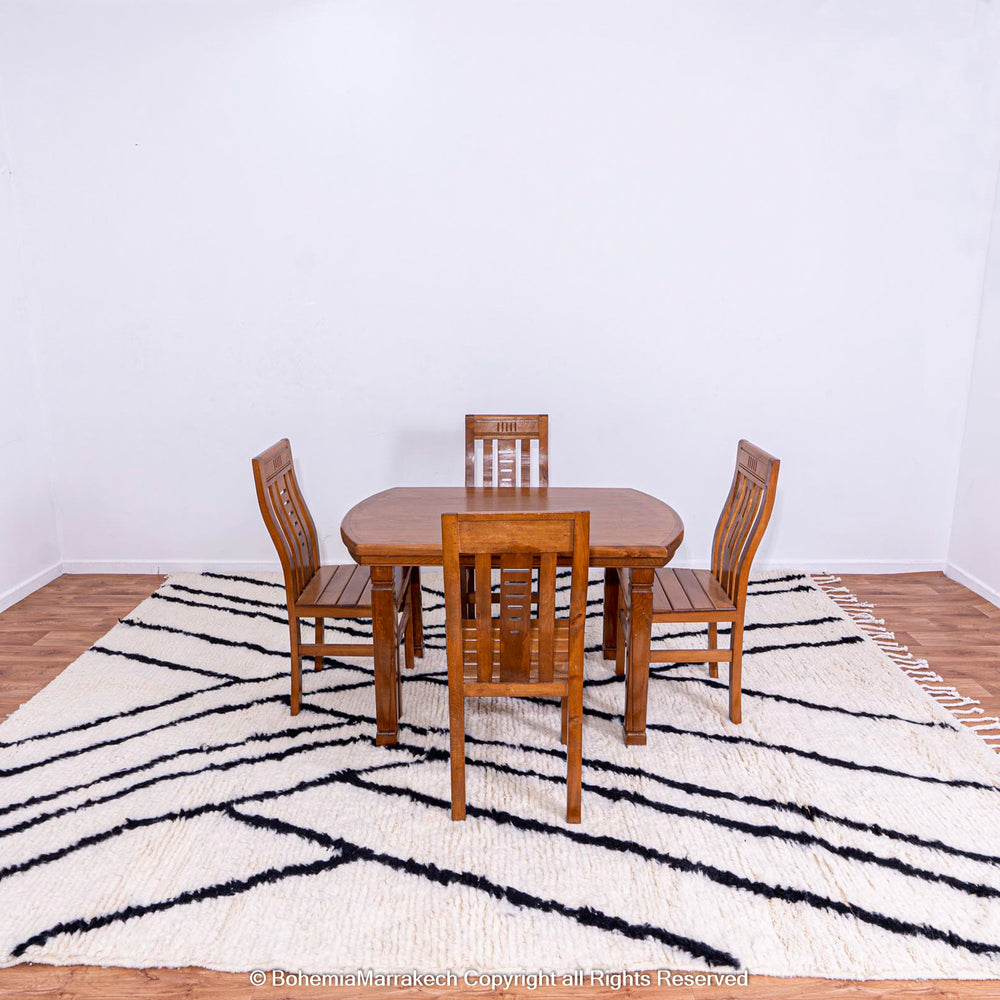 Black and white Beni Ourain Moroccan wool rug with criss-cross patterns under wooden dining table setting.