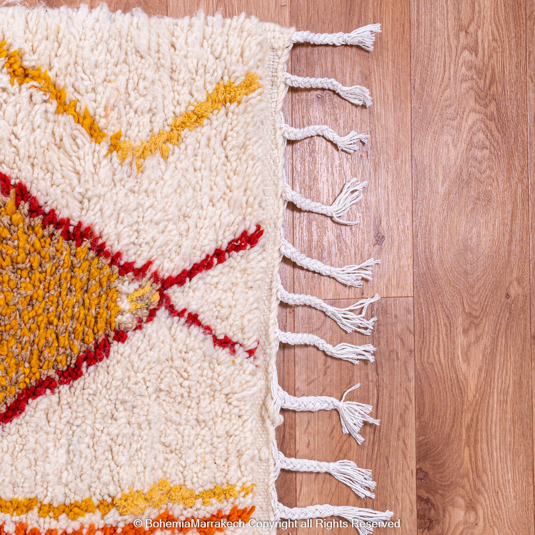 Handmade colorful Moroccan rug with bold tribal diamond pattern in orange, blue, red, and yellow on natural wool background