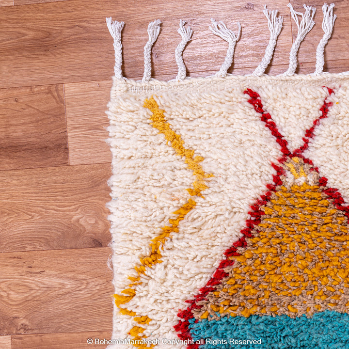 Handmade colorful Moroccan rug with bold tribal diamond pattern in orange, blue, red, and yellow on natural wool background