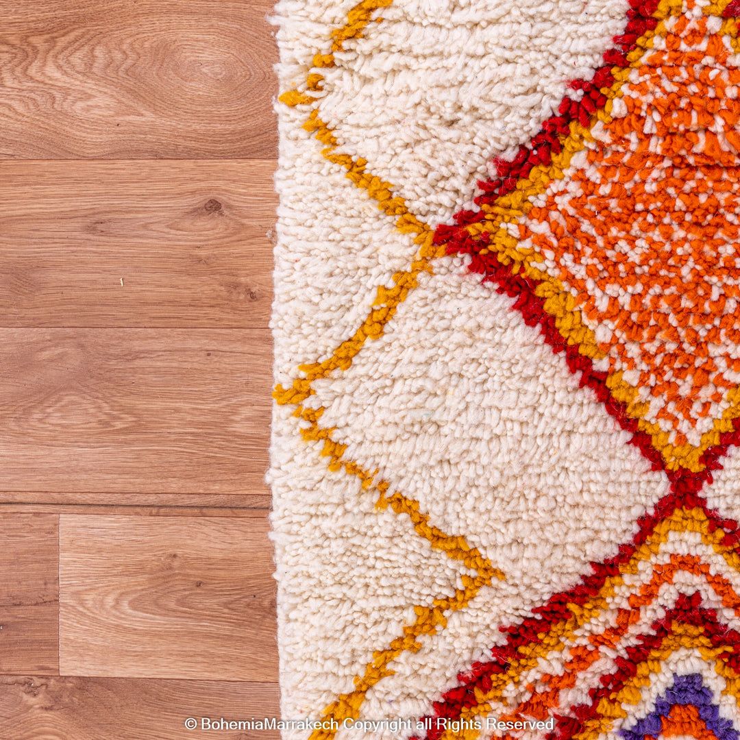 Handmade colorful Moroccan rug with bold tribal diamond pattern in orange, blue, red, and yellow on natural wool background