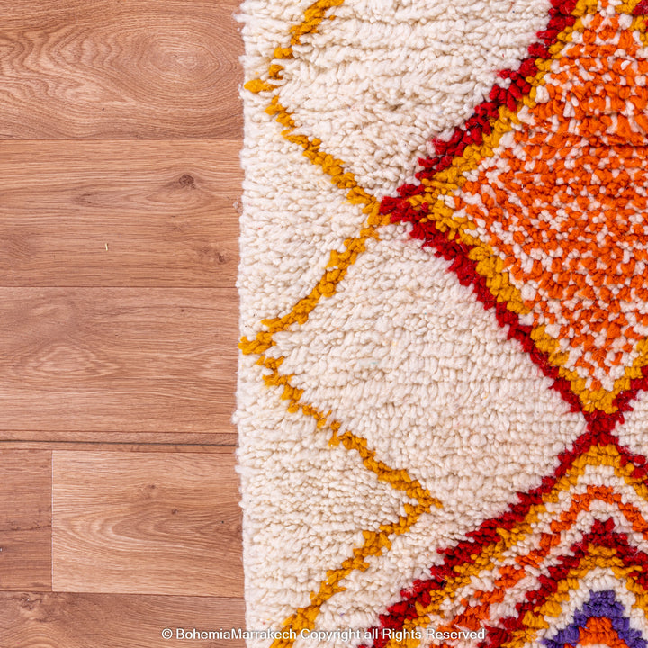 Handmade colorful Moroccan rug with bold tribal diamond pattern in orange, blue, red, and yellow on natural wool background