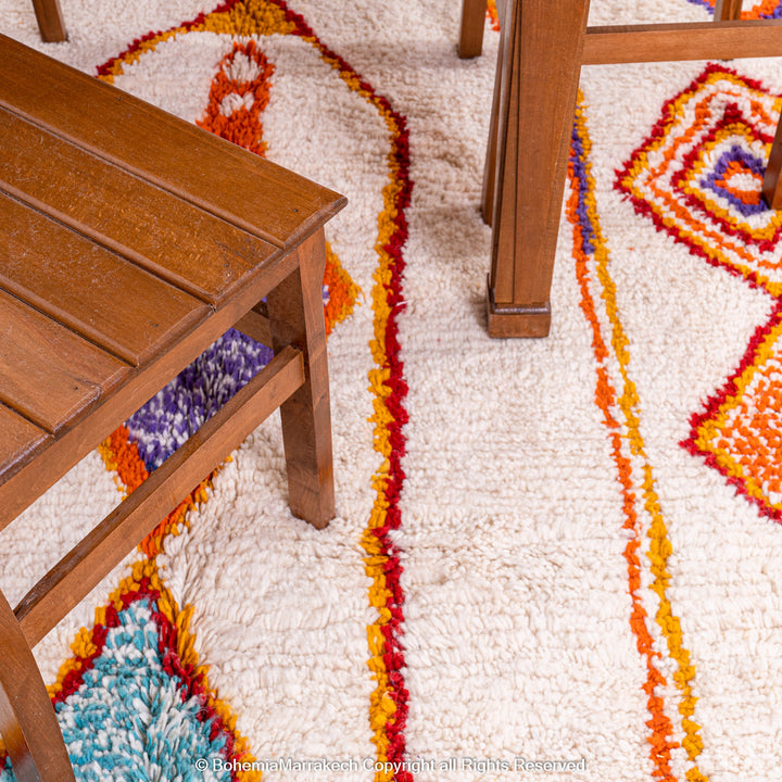 Handmade colorful Moroccan rug with bold tribal diamond pattern in orange, blue, red, and yellow on natural wool background