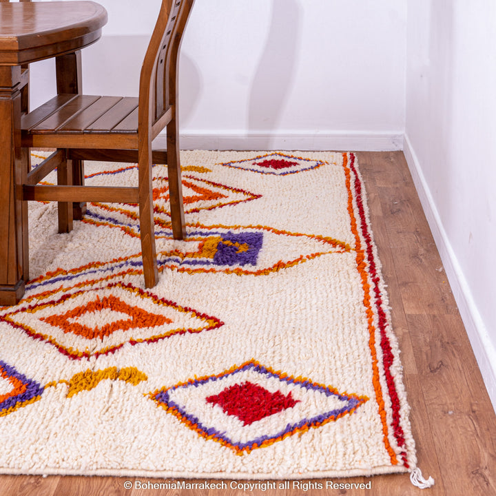 Handmade colorful Moroccan rug with bold tribal diamond pattern in orange, blue, red, and yellow on natural wool background