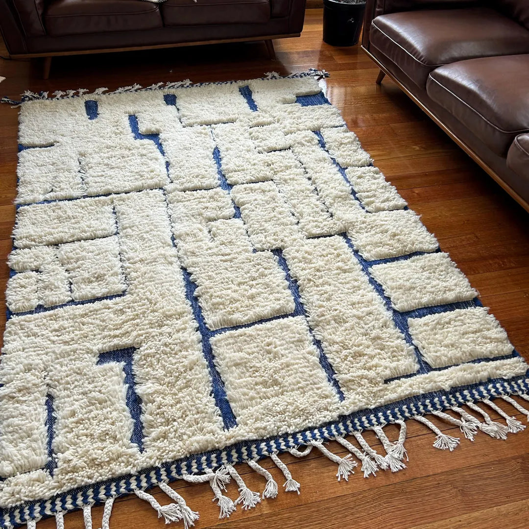 White and blue geometric patterned rug on a wooden floor with brown leather furniture.