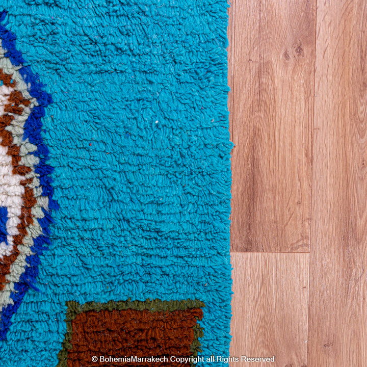 Vibrant blue Moroccan Berber rug with geometric patterns on wooden floor, showcasing traditional craftsmanship.