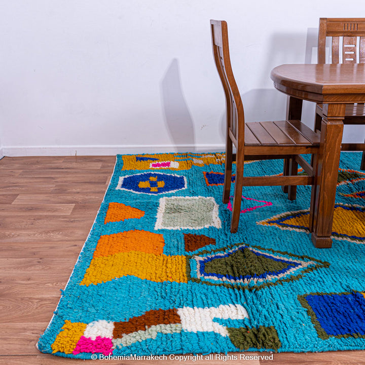 Blue Moroccan Berber rug with vibrant geometric symbols and tribal motifs in a dining room setting. Handmade from wool in Azilal style.