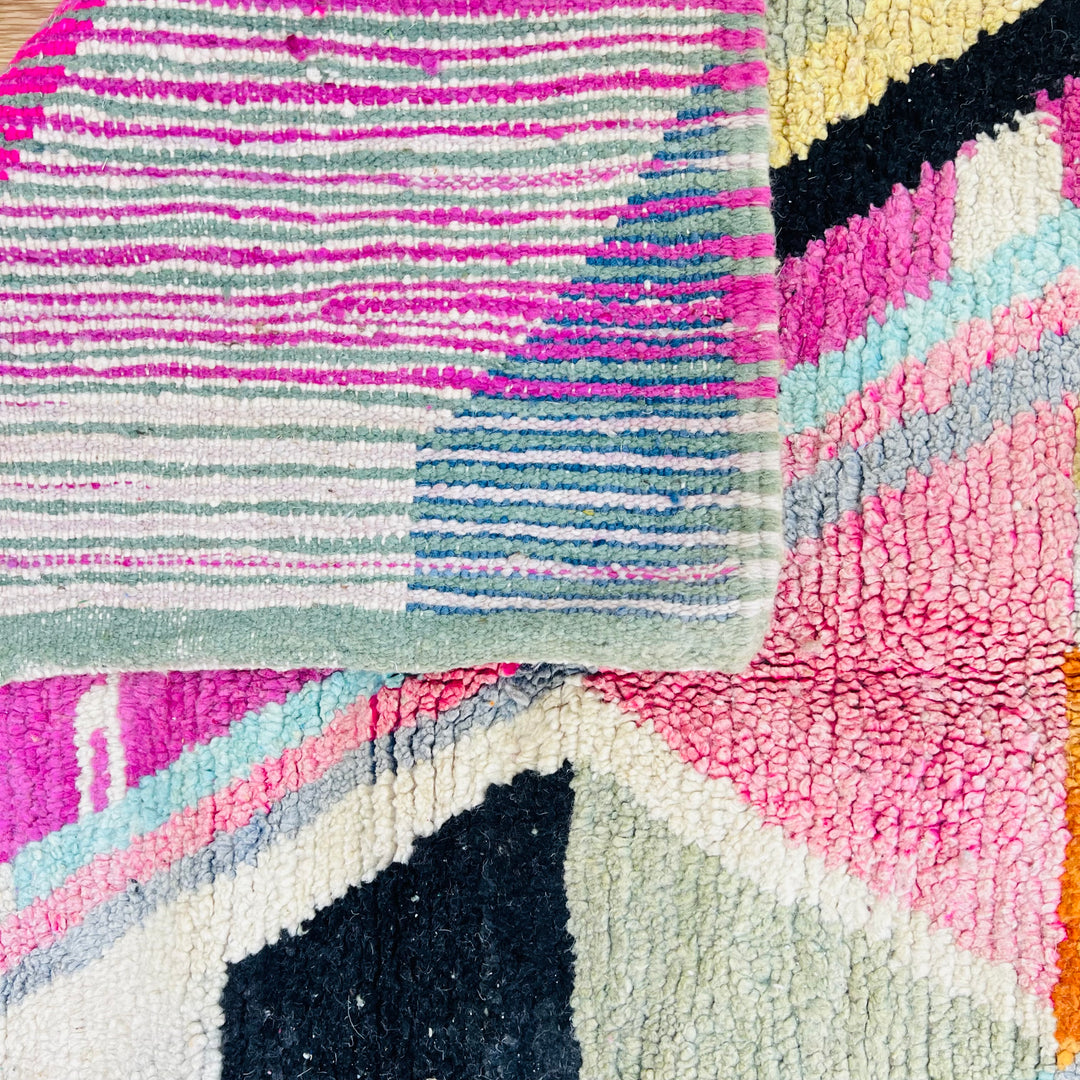 Close-up of vibrant vintage Moroccan rug with geometric patterns in pink, green, blue, and black, handwoven by Berber artisans.