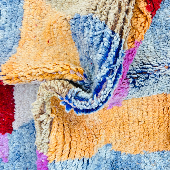 Close-up of a colorful diamond vintage Moroccan rug with red, coral, ochre, beige, and blue harlequin pattern.
