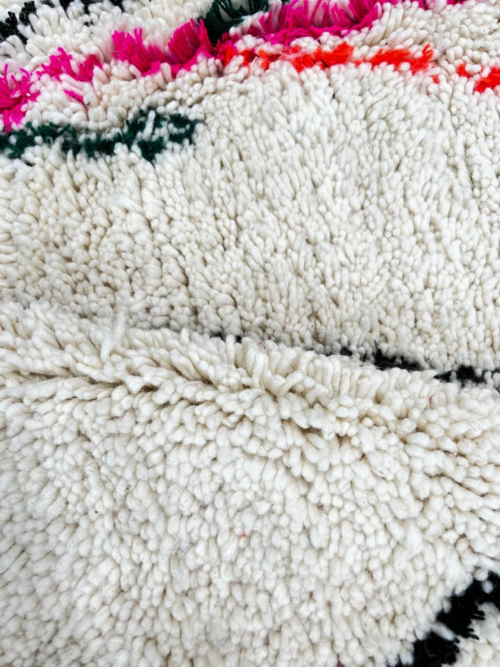 Minimalist Moroccan wool rug with black diamond lines and colorful details on cream background, handmade by Berber artisans