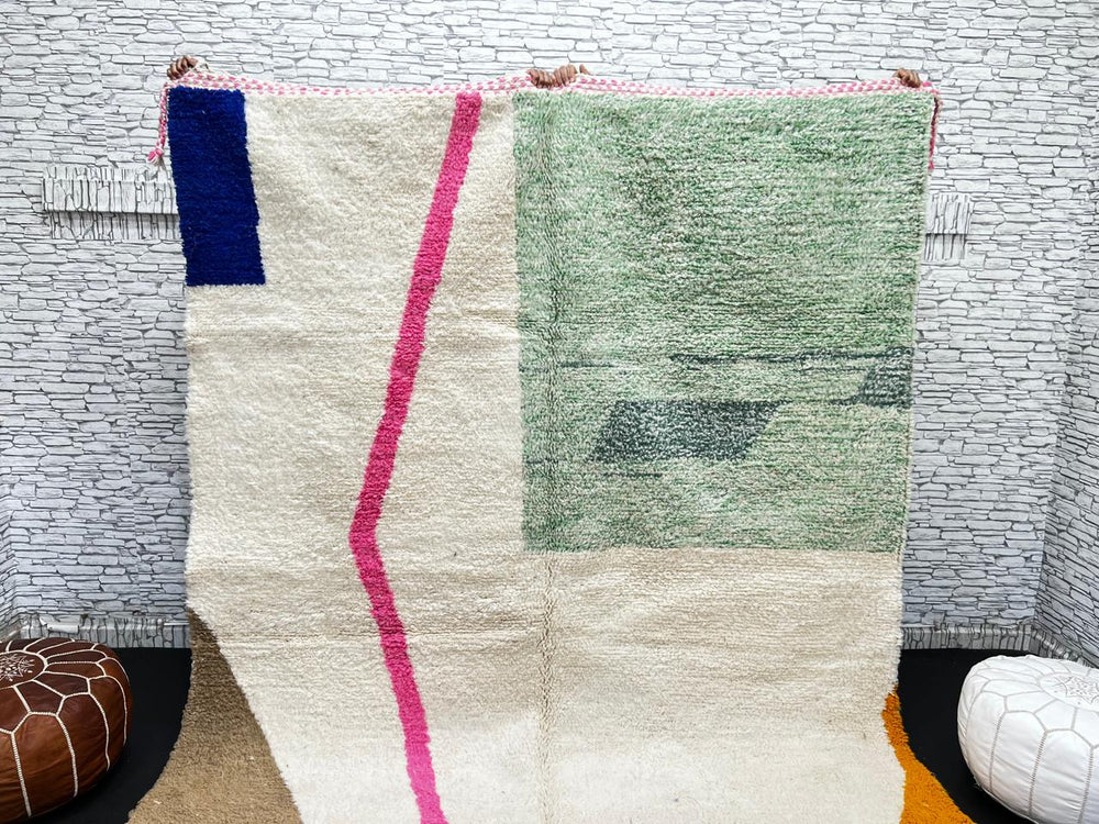 Modern Moroccan wool rug with abstract minimalist design featuring pink, green, and blue geometric accents, handmade by Berber artisans