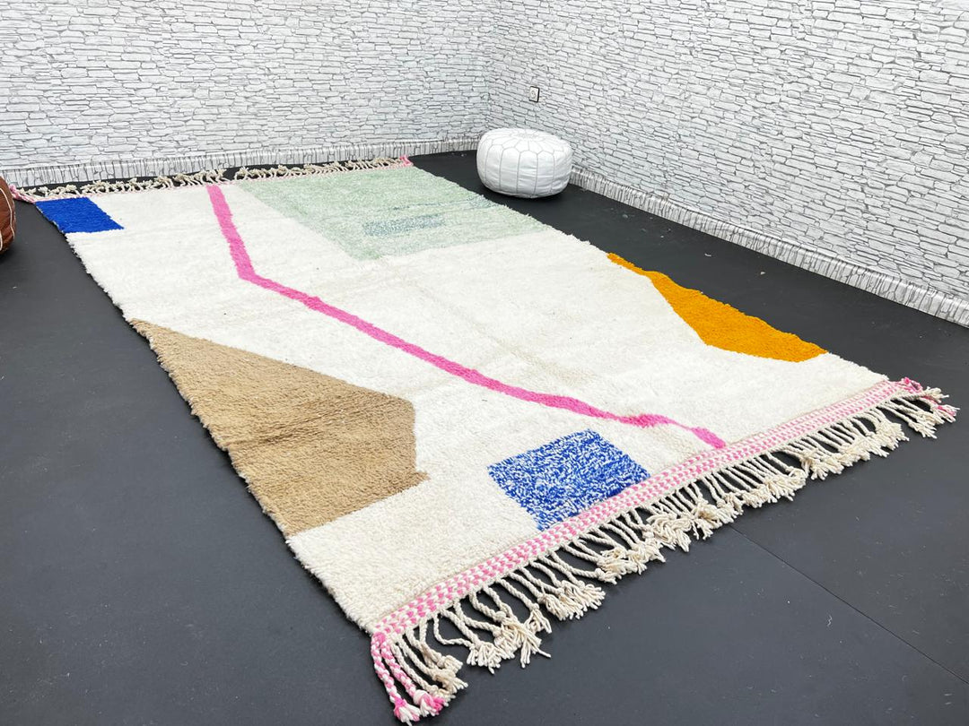 Modern Moroccan wool rug with abstract minimalist design featuring pink, green, and blue geometric accents, handmade by Berber artisans