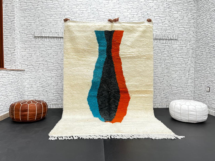 Beige Moroccan wool rug with central abstract design in blue, black, and orange, handmade by Berber artisans