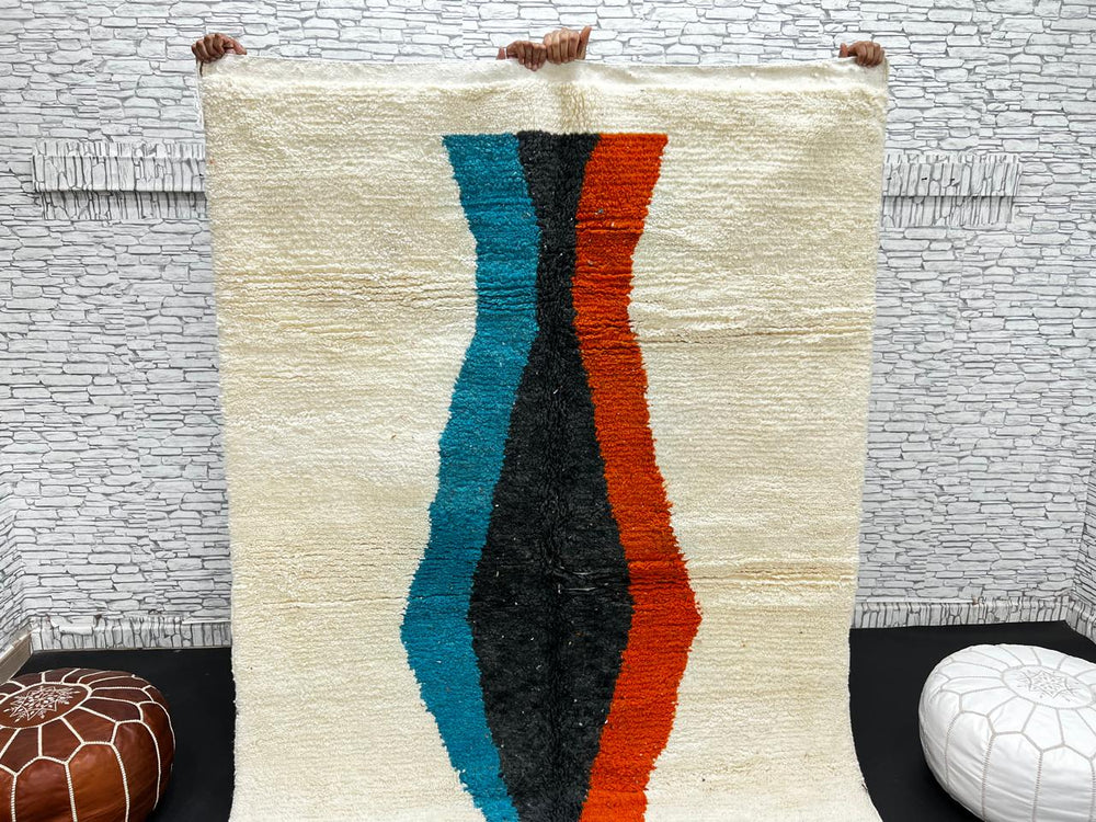 Beige Moroccan wool rug with central abstract design in blue, black, and orange, handmade by Berber artisans