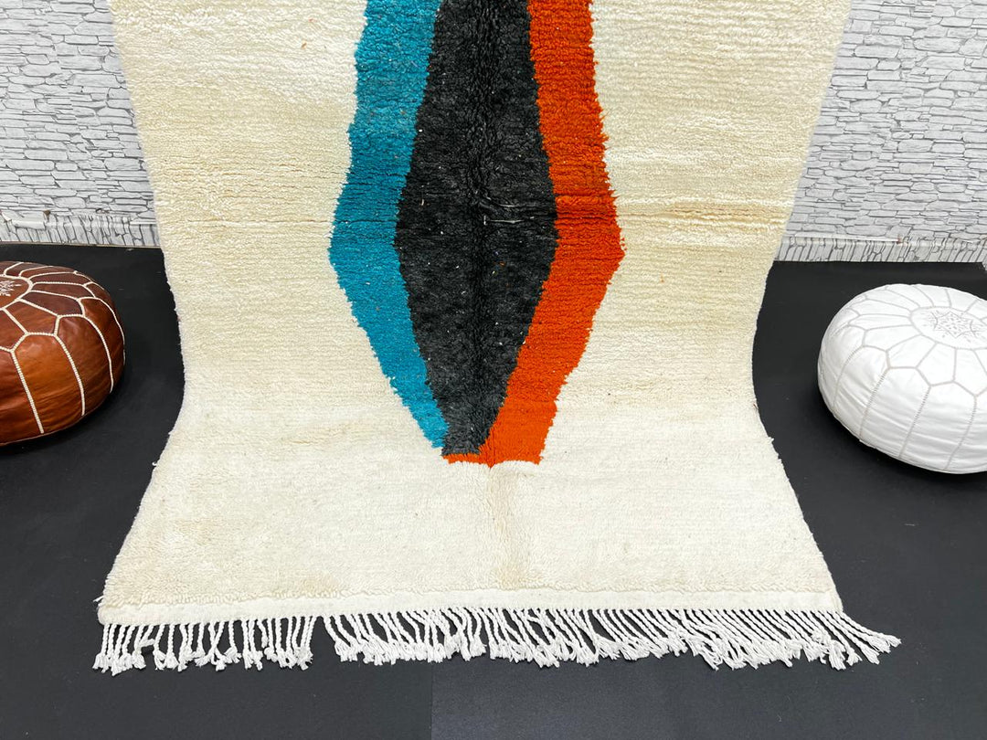 Beige Moroccan wool rug with central abstract design in blue, black, and orange, handmade by Berber artisans