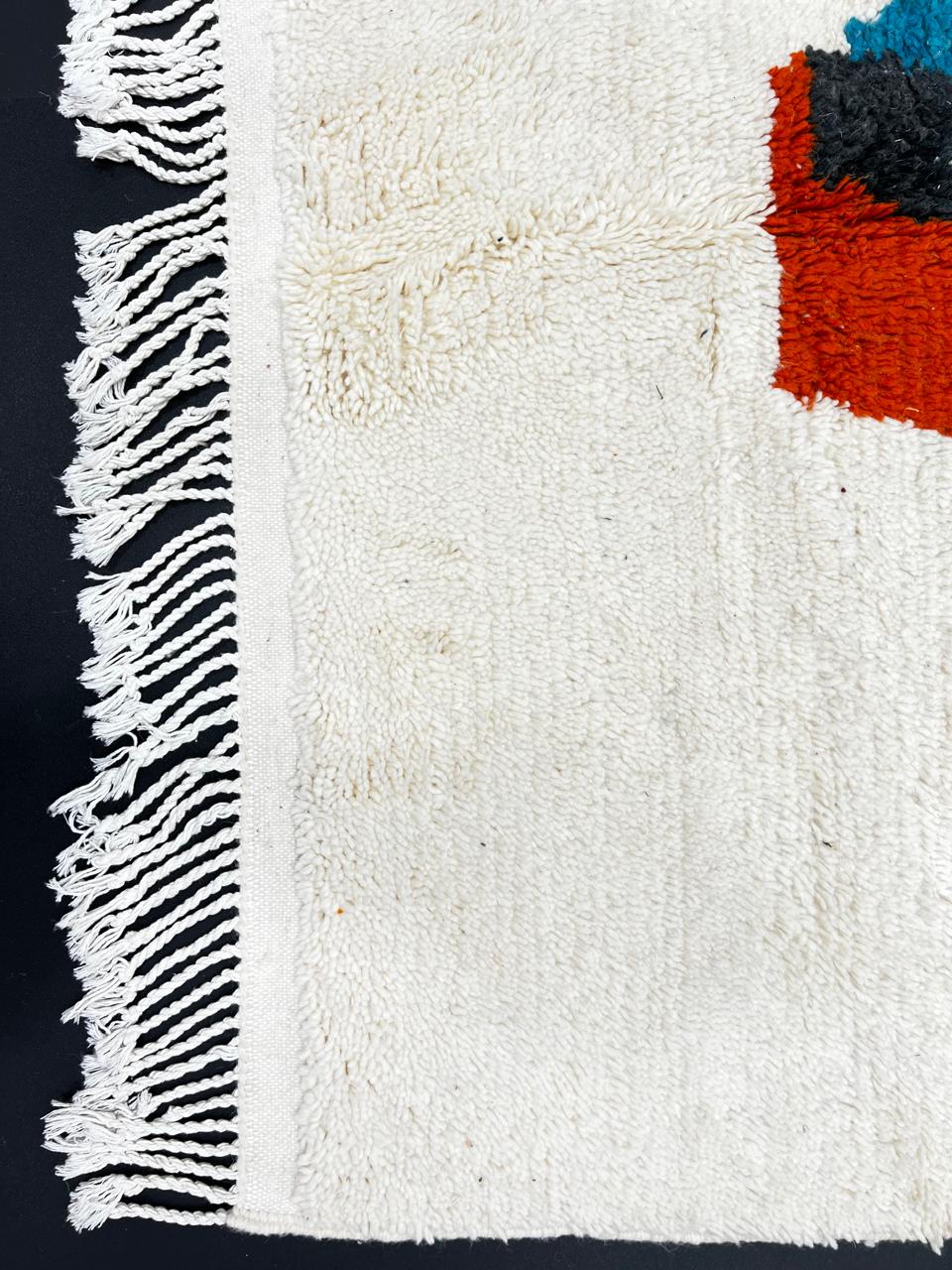 Beige Moroccan wool rug with central abstract design in blue, black, and orange, handmade by Berber artisans