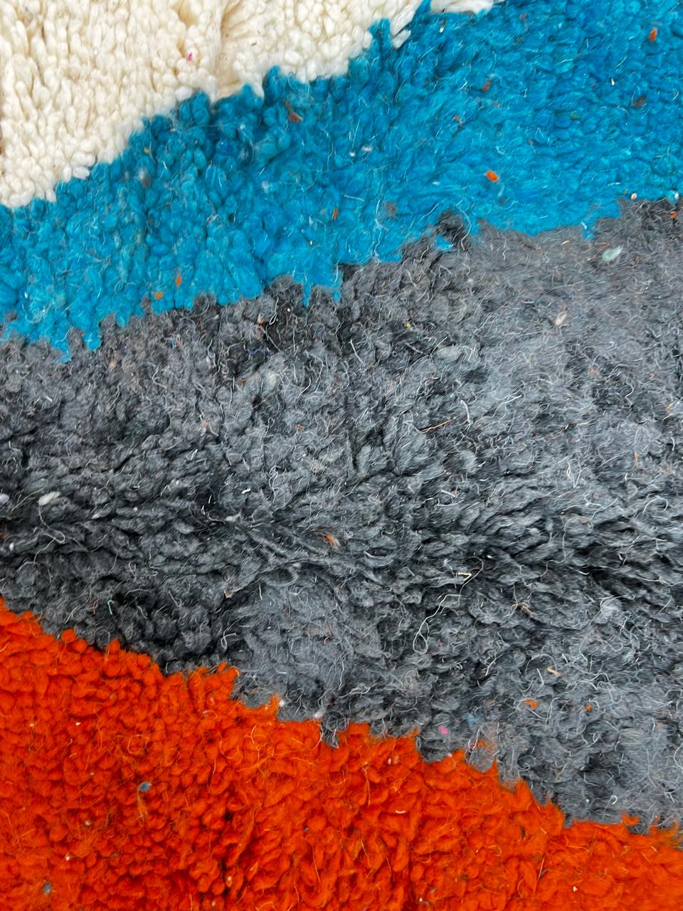 Beige Moroccan wool rug with central abstract design in blue, black, and orange, handmade by Berber artisans