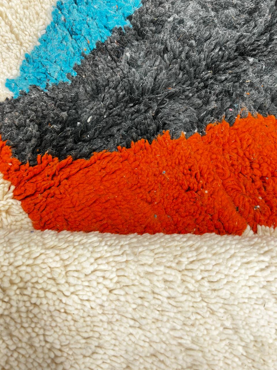 Beige Moroccan wool rug with central abstract design in blue, black, and orange, handmade by Berber artisans