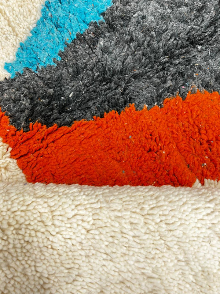 Beige Moroccan wool rug with central abstract design in blue, black, and orange, handmade by Berber artisans