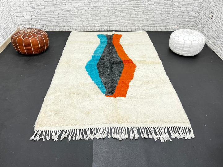 Beige Moroccan wool rug with central abstract design in blue, black, and orange, handmade by Berber artisans