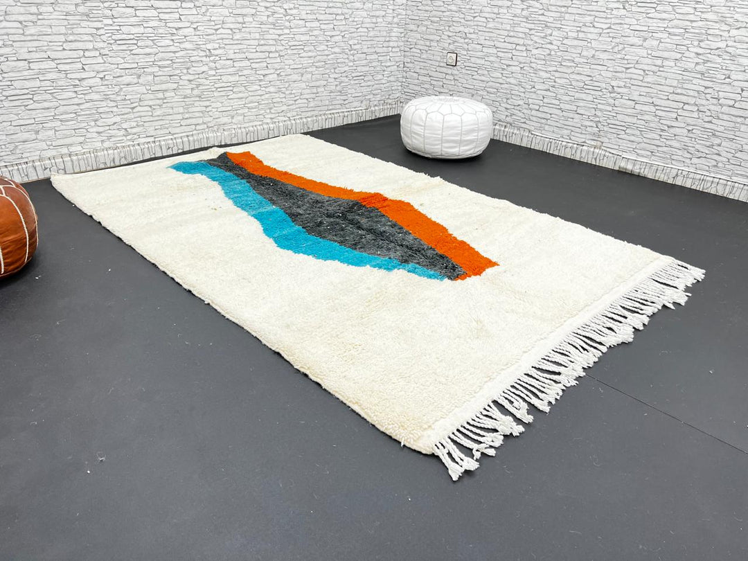 Beige Moroccan wool rug with central abstract design in blue, black, and orange, handmade by Berber artisans