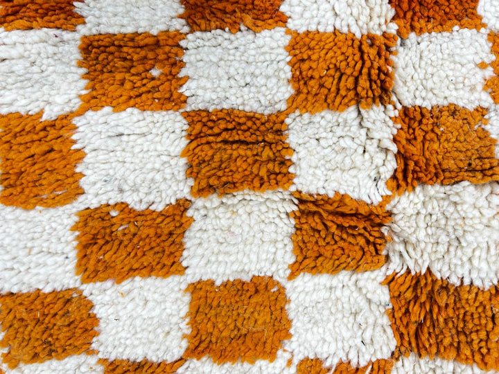 Handmade round Moroccan wool rug with orange and white checkerboard pattern on white background