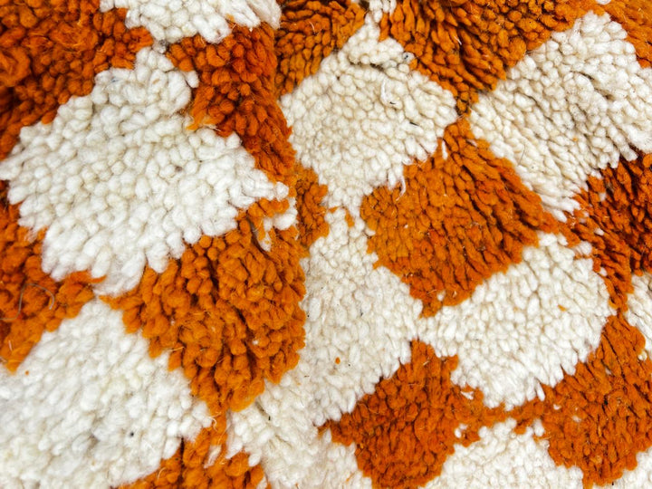 Handmade round Moroccan wool rug with orange and white checkerboard pattern on white background