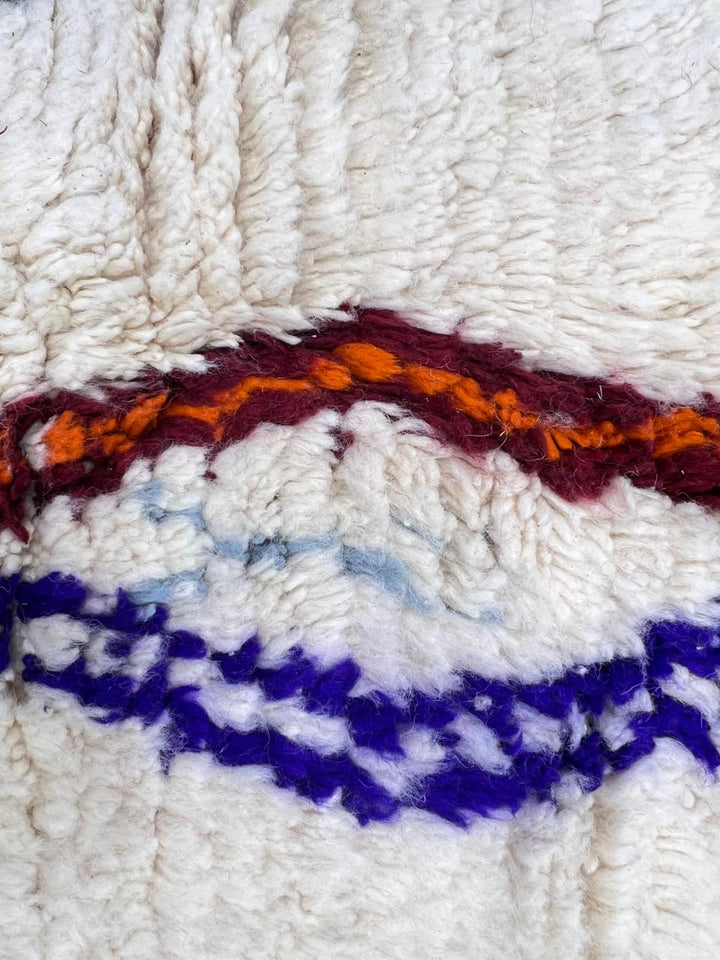 Handmade colorful round Moroccan wool rug with an ivory background and blue, green, orange, burgundy, and gray Berber motifs.