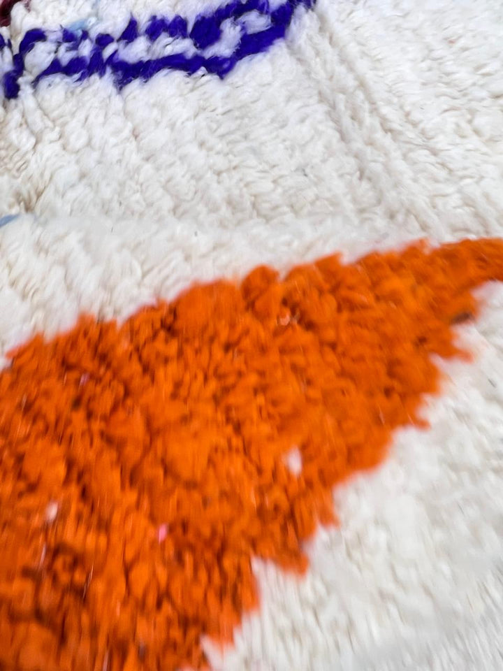Handmade colorful round Moroccan wool rug with an ivory background and blue, green, orange, burgundy, and gray Berber motifs.