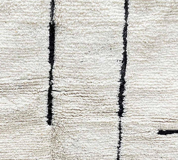 Round Moroccan rug with minimalist black abstract line pattern on a cream-white wool base