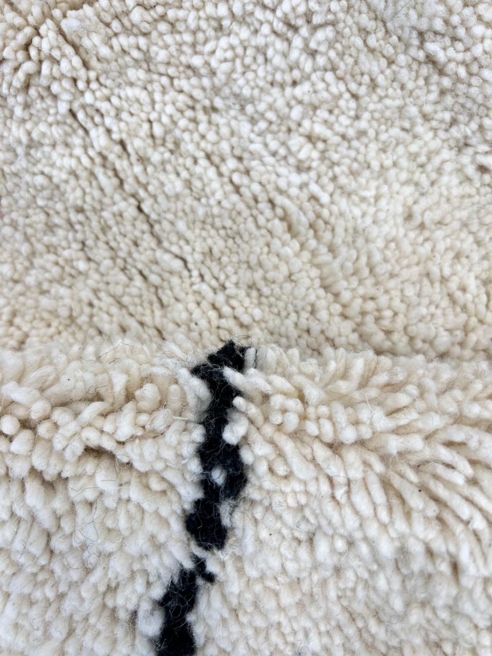 Round Moroccan wool rug in natural ivory with a minimalist black diamond lattice pattern, handwoven in a soft.