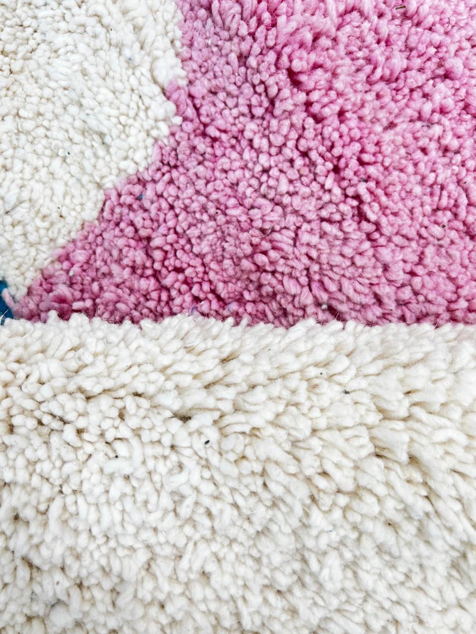 Handmade round Moroccan wool rug with abstract modern design on an white base, featuring orange, black, pink, teal, and beige shapes.