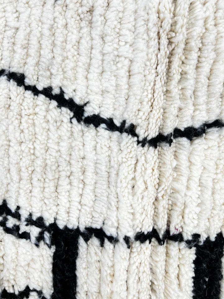 Handmade round Moroccan wool rug with traditional Berber symbols, featuring black geometric motifs on an white wool base.