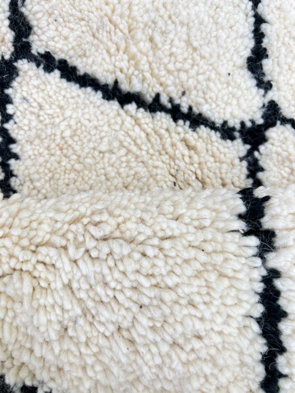 White round Moroccan wool rug with black diamond line pattern.