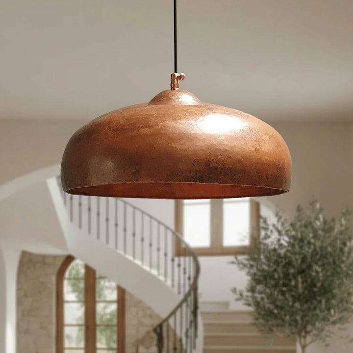 Copper pendant light hanging in a room with a staircase and plant in the background